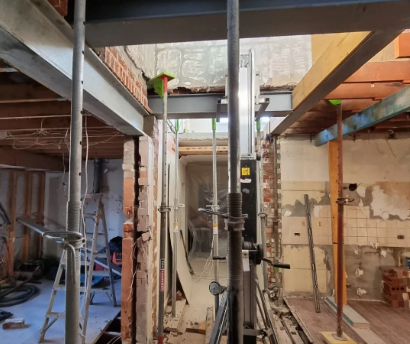 Interior construction site with scaffolding, exposed beams, and work lights in a narrow unfinished room