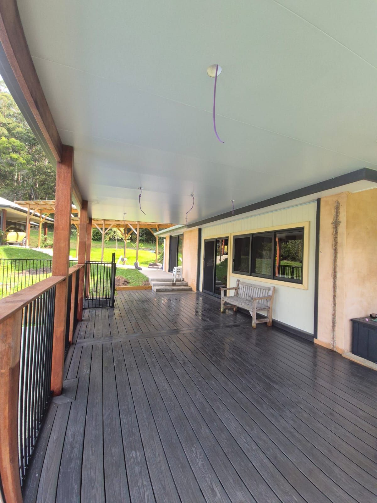 Covered wooden porch with dark floorboards, railing, and bench beside a cream house wall.