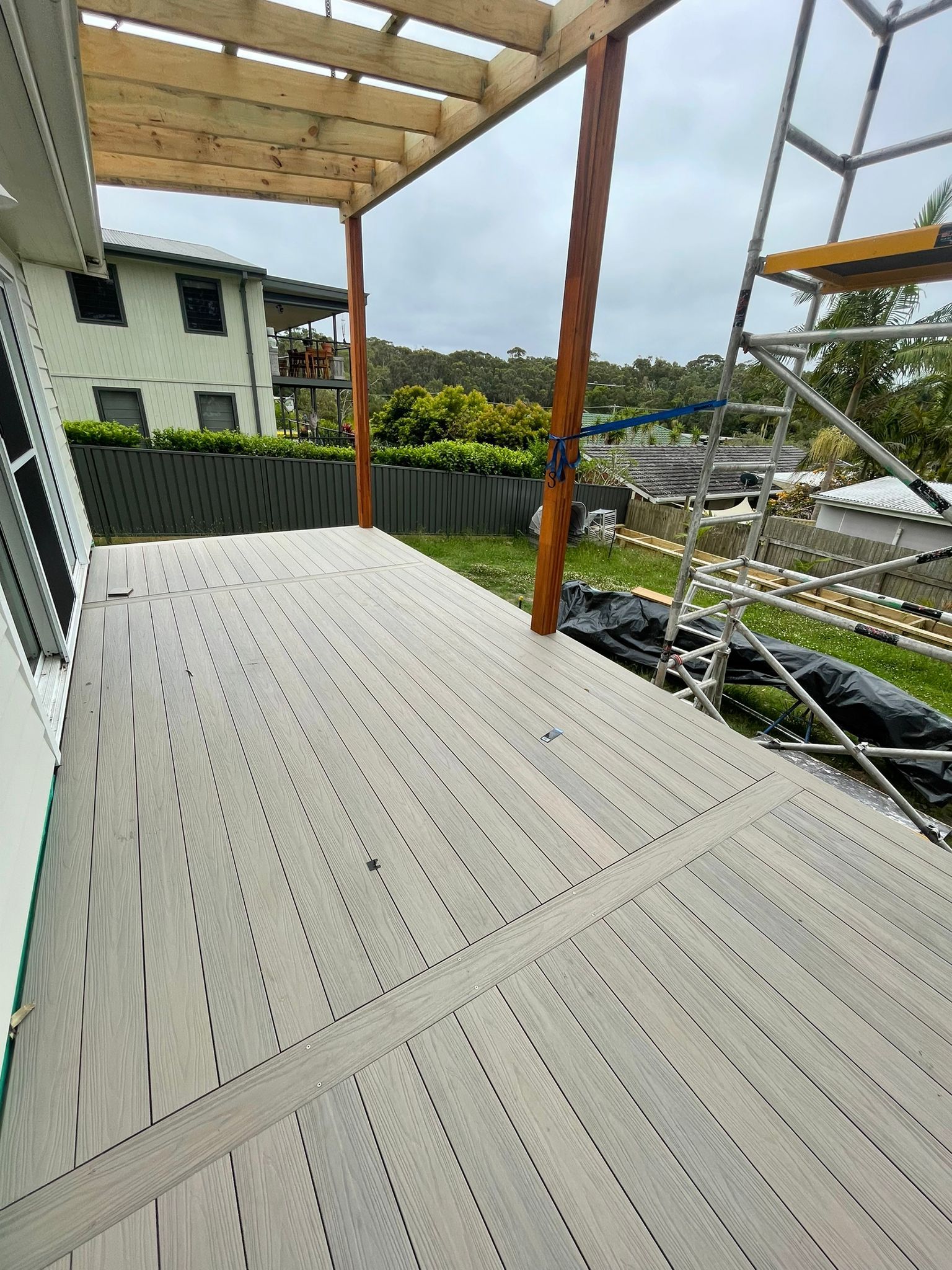 Covered wooden deck with metal railings overlooking a yard and distant houses