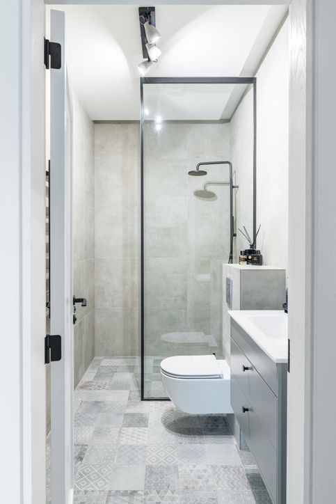 A small, modern bathroom with a glass shower, toilet, and vanity. Gray and white tones dominate.