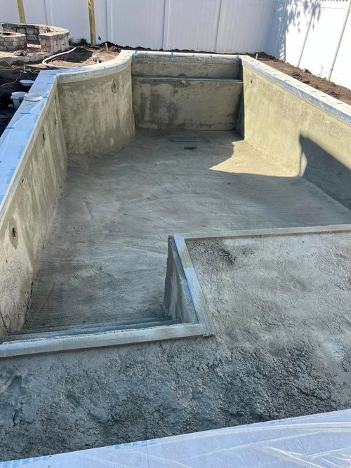 Empty concrete swimming pool under construction, with blue coping and unfinished walls.