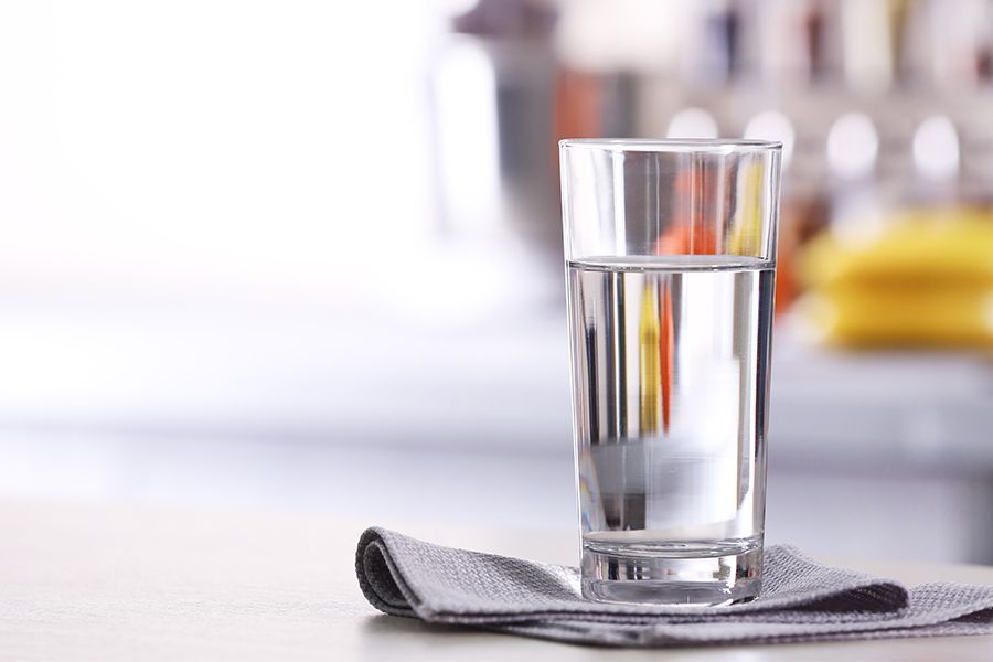 Glass of water on a gray napkin, set on a light-colored surface in a bright kitchen.
