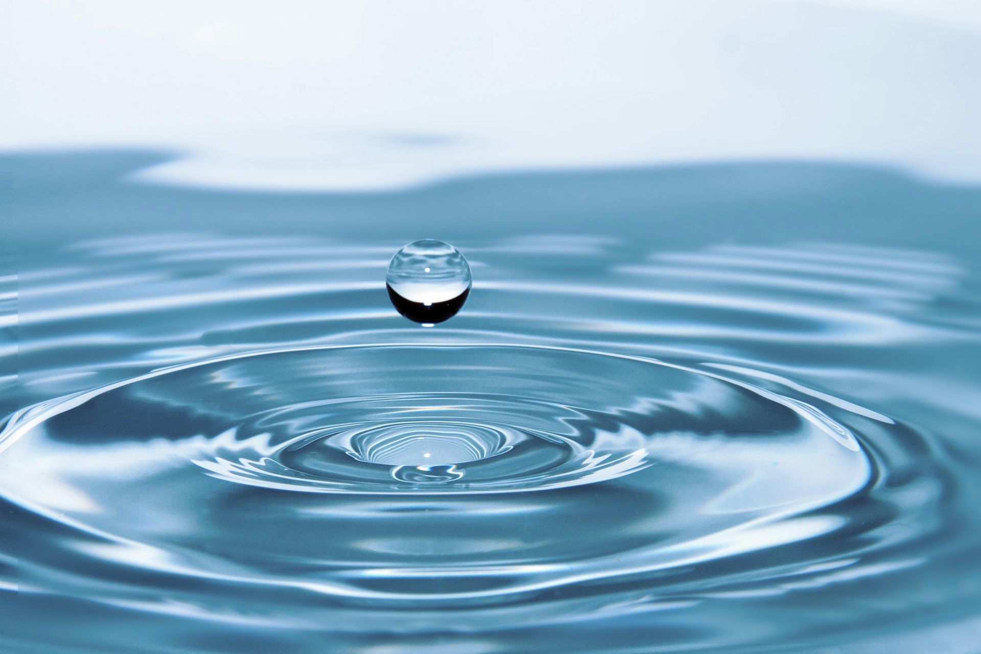 Water droplet falling into calm blue water, creating concentric ripples