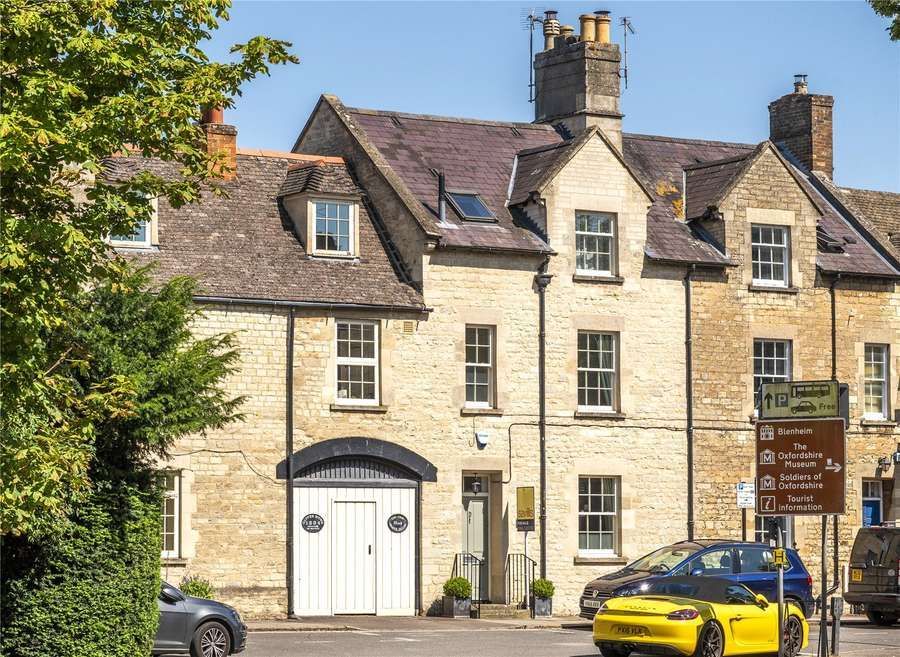 Stone building with arched doorway and white doors, cars parked in front, signpost on the right.