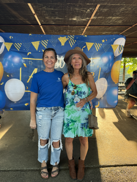 Two women are posing for a picture in front of a banner with balloons on it