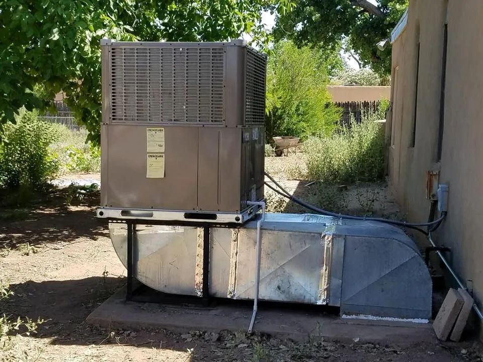 Large outdoor HVAC unit beside a building, sitting on metal supports in a shaded yard.