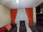 Sala de estar con cortinas naranjas, sofá oscuro, sillón y mueble para la televisión junto a la ventana.