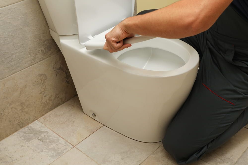 A Man Is Kneeling Down Next to A Toilet in A Bathroom — Blair Merlehan Plumbing in Wagga Wagga, NSW