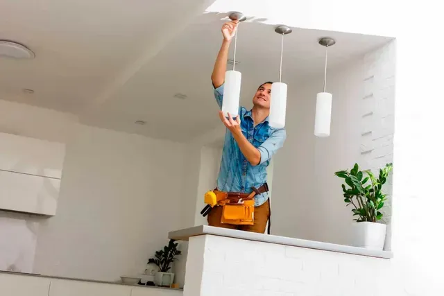 Person standing on a kitchen counter changing a ceiling light bulb using a tool belt