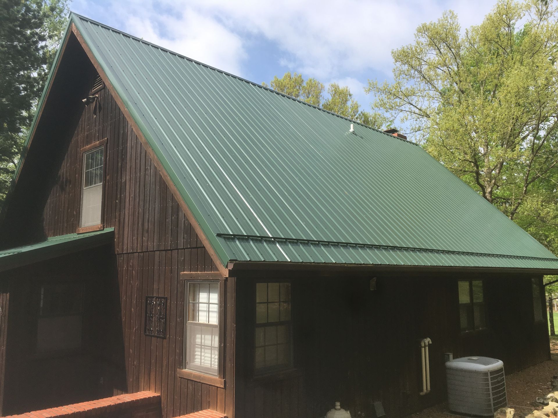 Small rustic cabin with dark wood walls and a green metal roof under a partly cloudy sky.