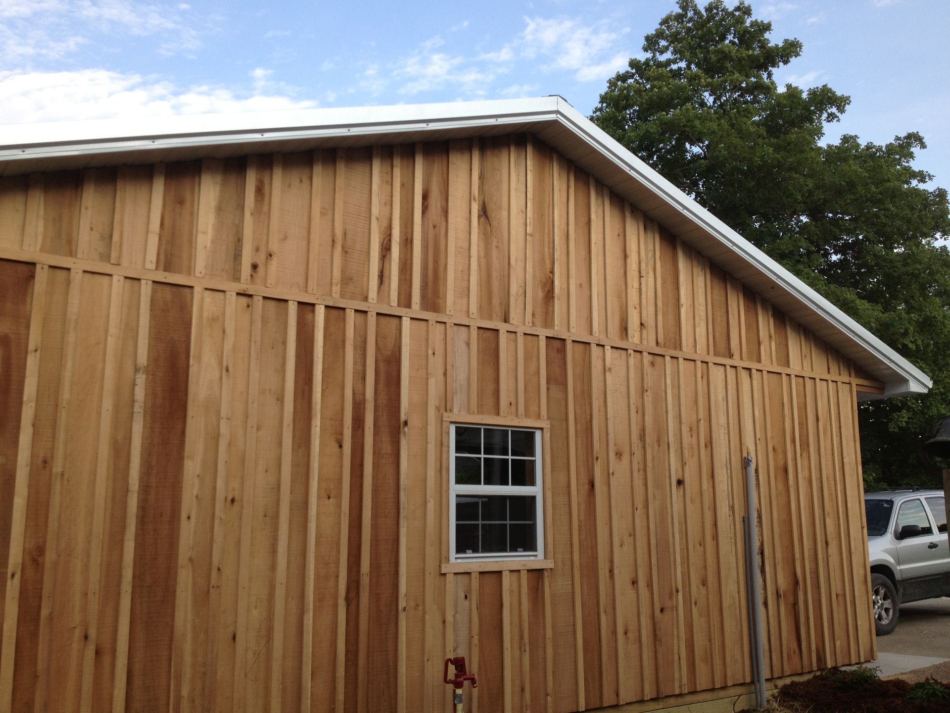 Wooden barn-like shed with a metal roof and a small window under a partly cloudy sky