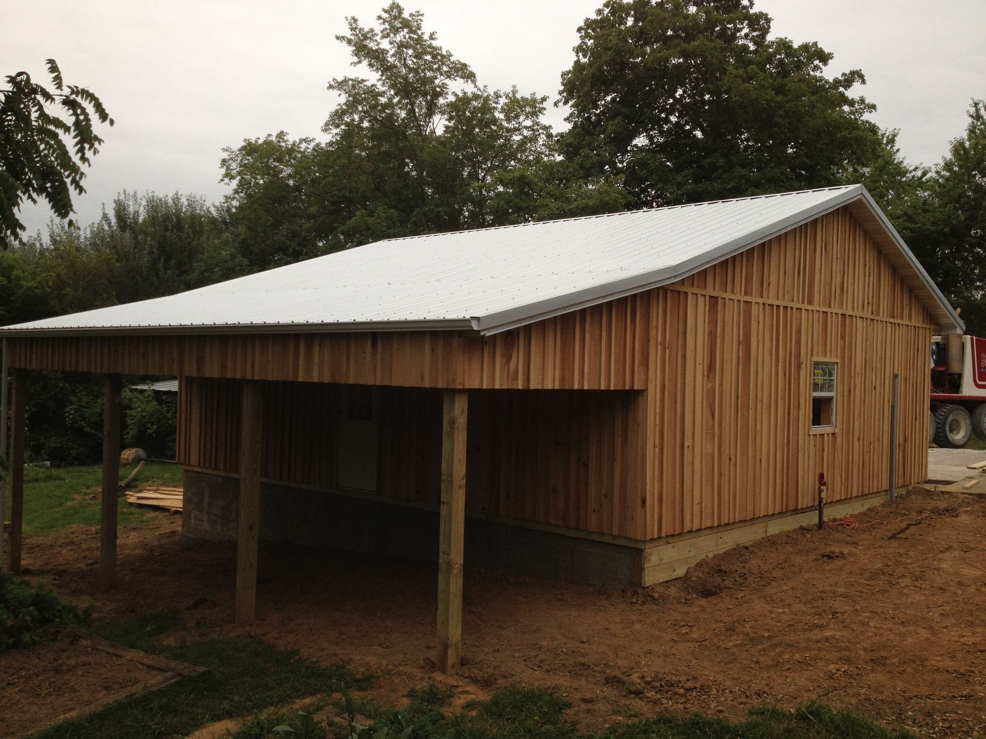 Small wooden shed with a metal roof and open front in a rural, tree-lined yard.