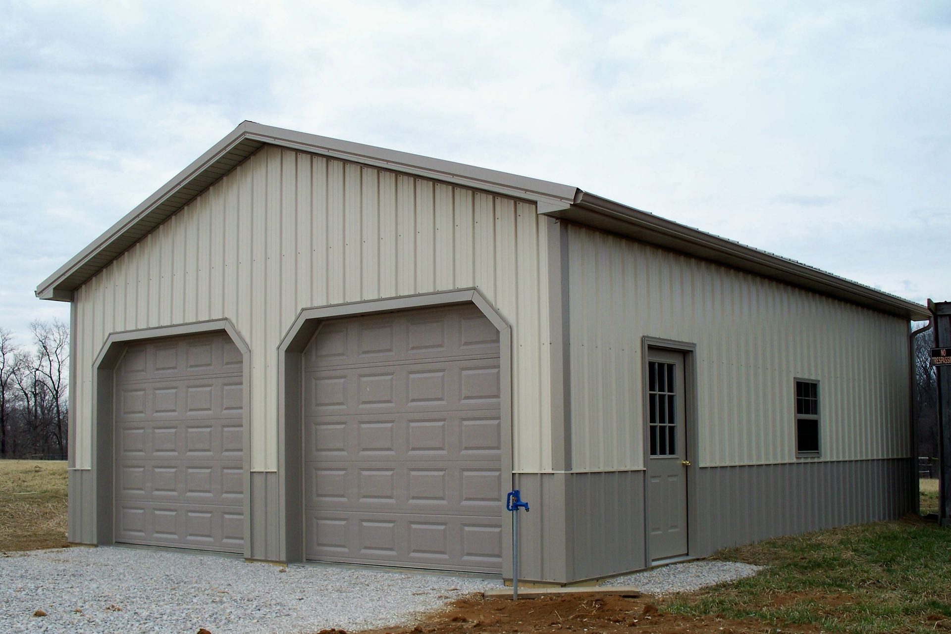 Beige two-car garage with gray trim and gravel driveway under a cloudy sky