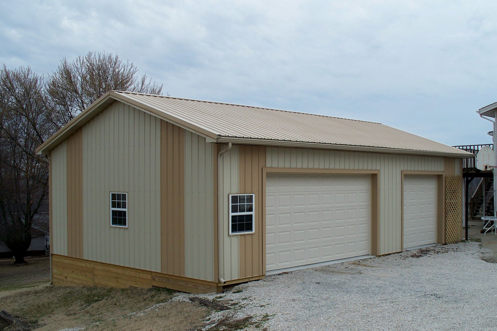 Beige metal garage with two white doors and a small side window on a gravel driveway