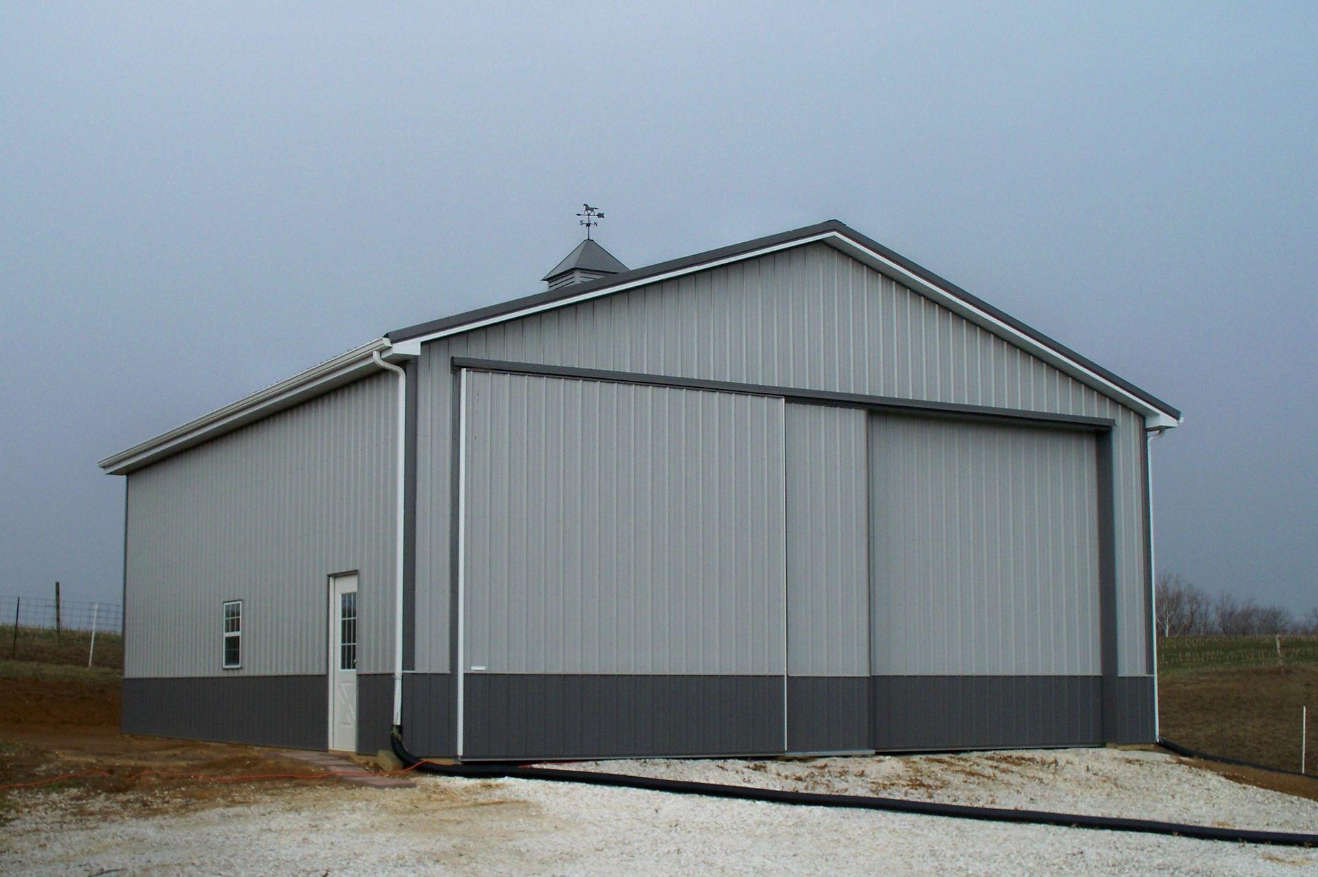 Gray metal barn with a large sliding door in a rural field under an overcast sky