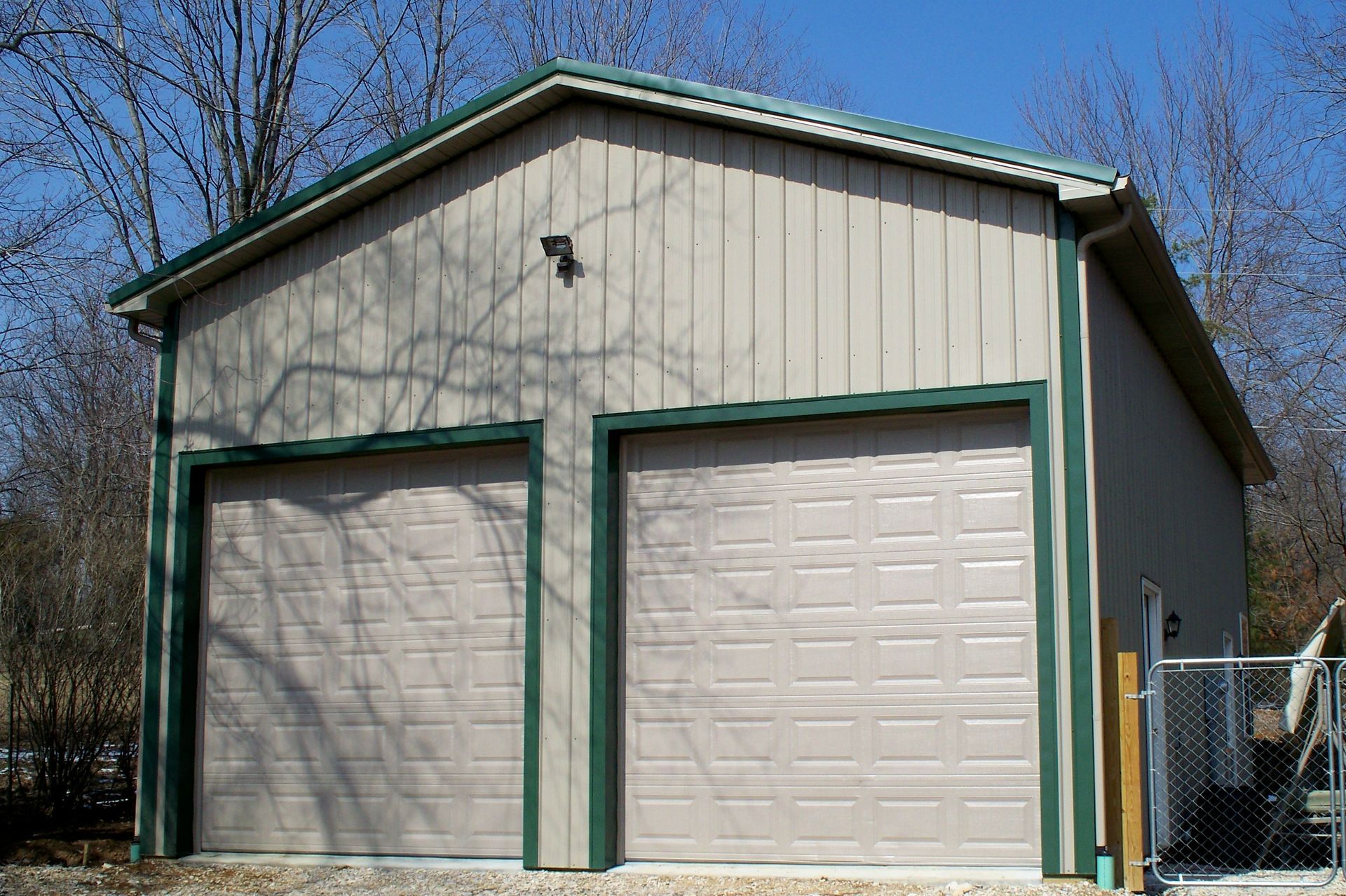 Two-door beige garage with green trim and closed white doors under a blue sky