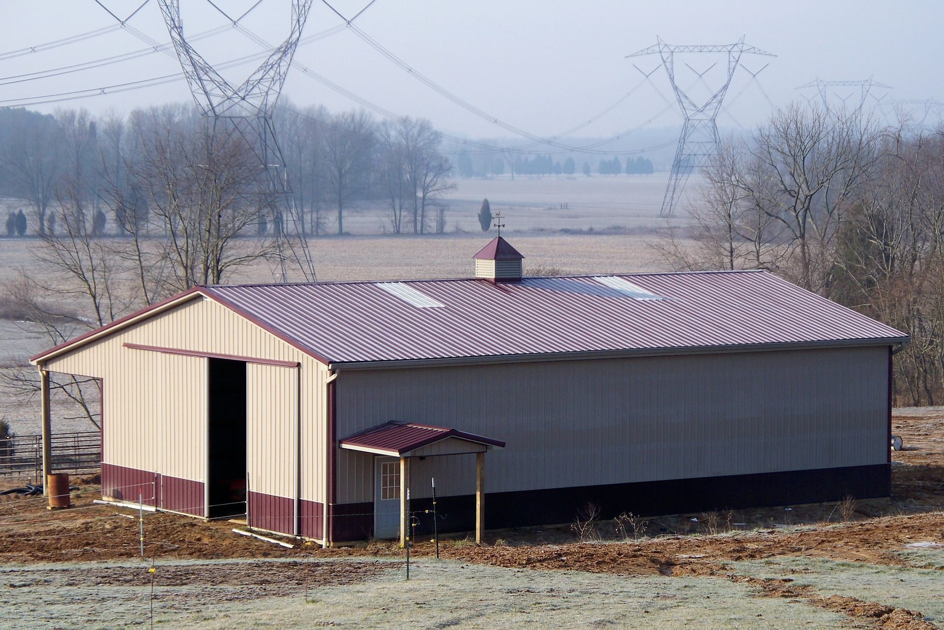 Rural barn with red metal roof and beige siding in a foggy field, with power lines overhead