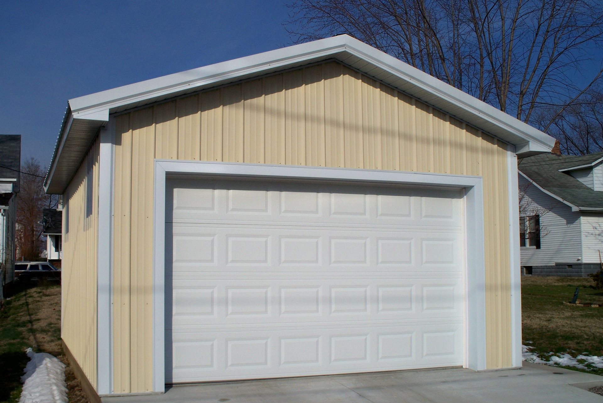 White garage door on a beige detached garage under a clear blue sky.