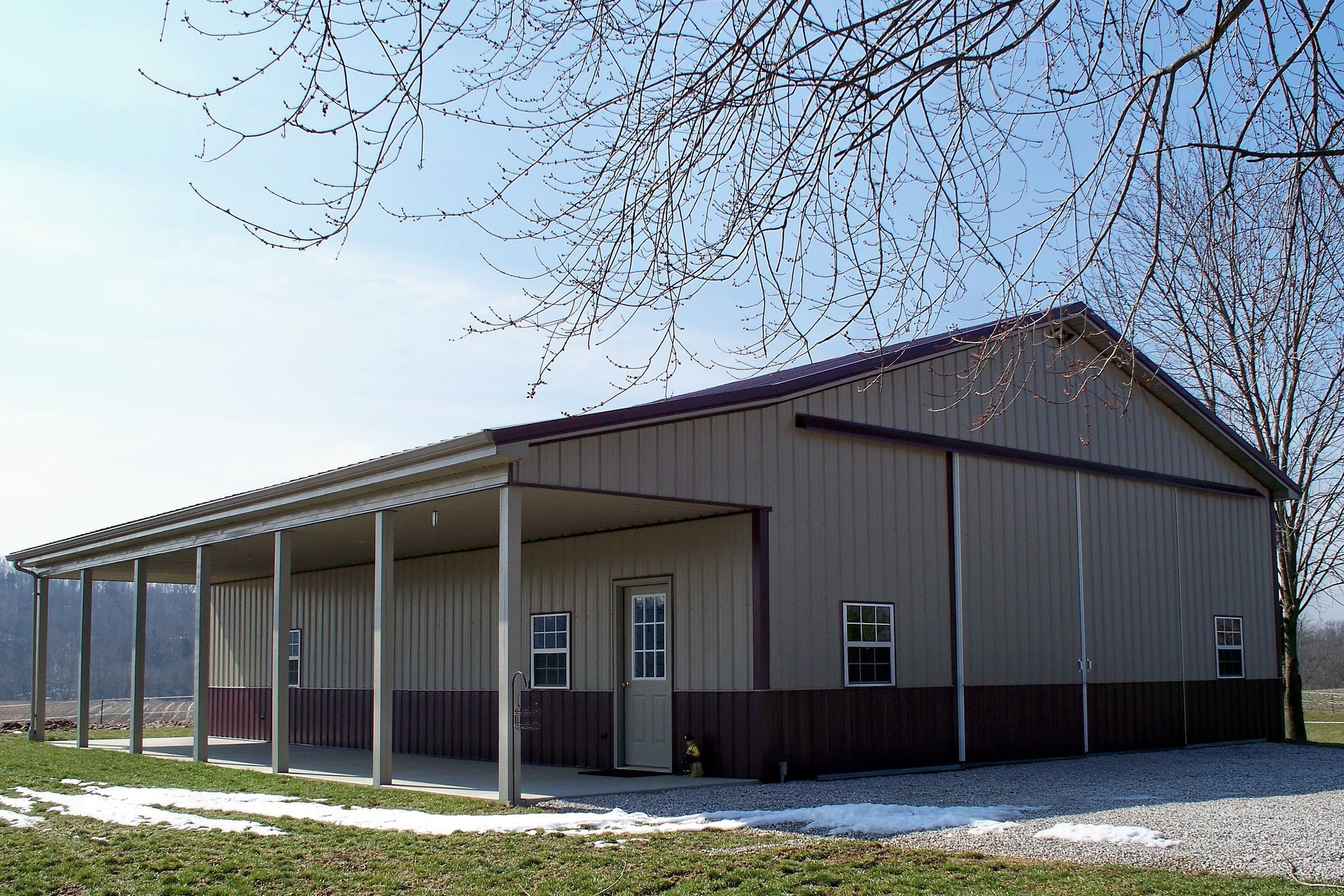 Large gray barn-like building with a covered porch and columns on a snowy rural lot