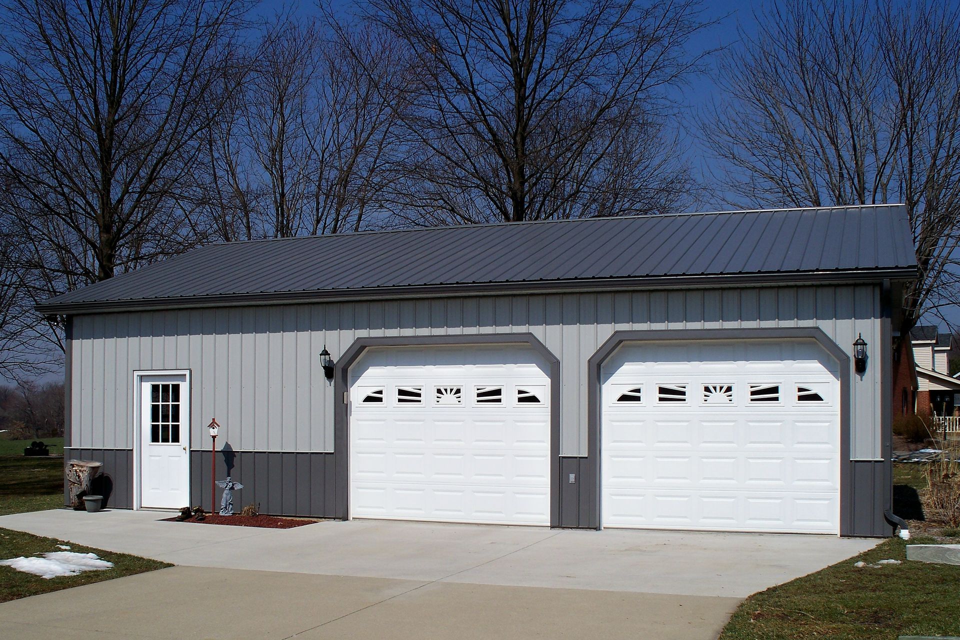 Gray metal garage with two white doors and a side entrance under a dark roof on a sunny day