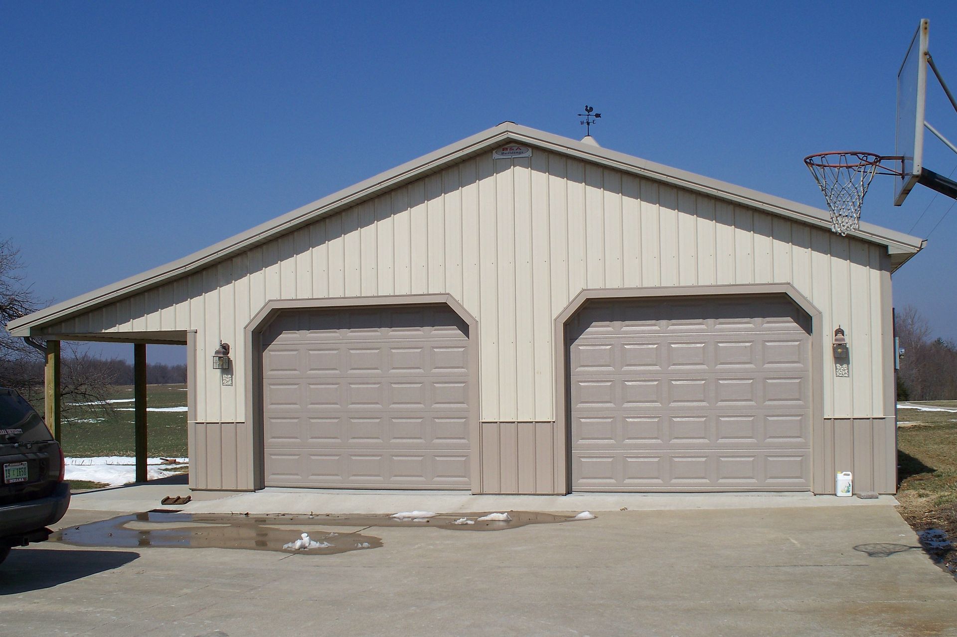 Beige two-car garage with tan doors under a blue sky, fronted by a concrete driveway