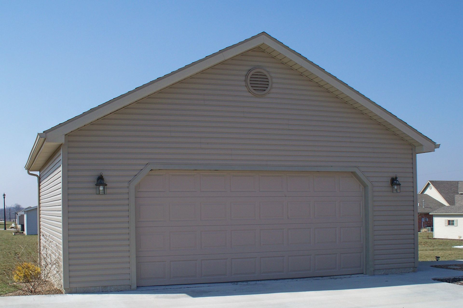 Detached two-car garage with beige siding and snow on the ground under a clear sky