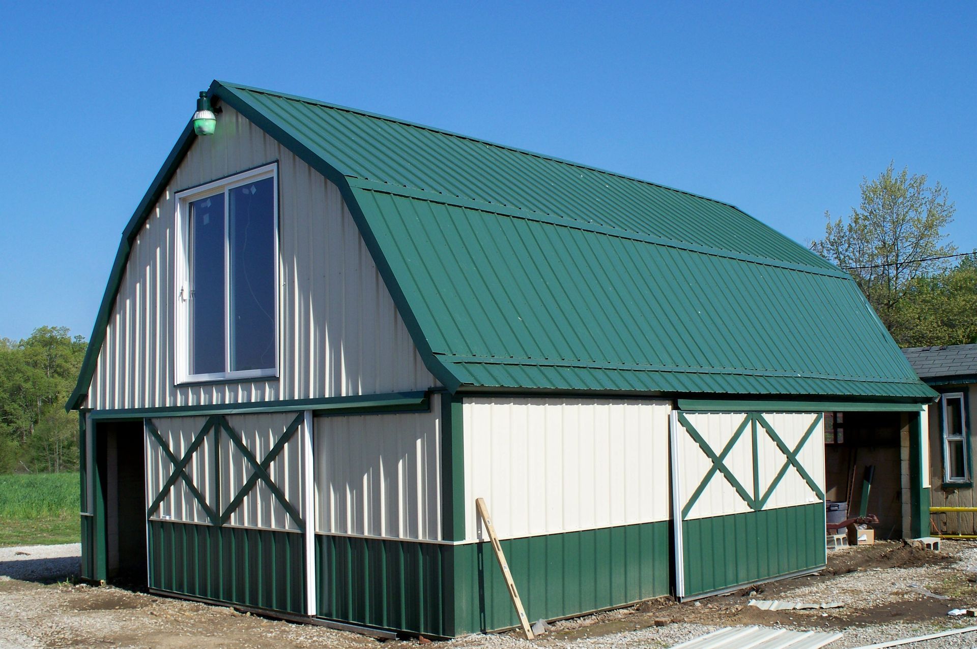 Green-roofed white barn with green trim and large sliding doors on a gravel lot under a clear sky