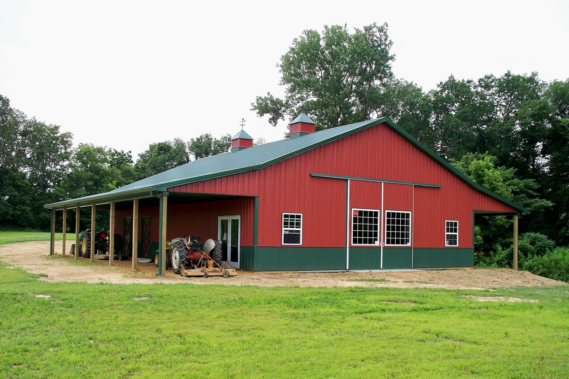 Red barn-style farmhouse with green roof and porch, set in a grassy rural yard.