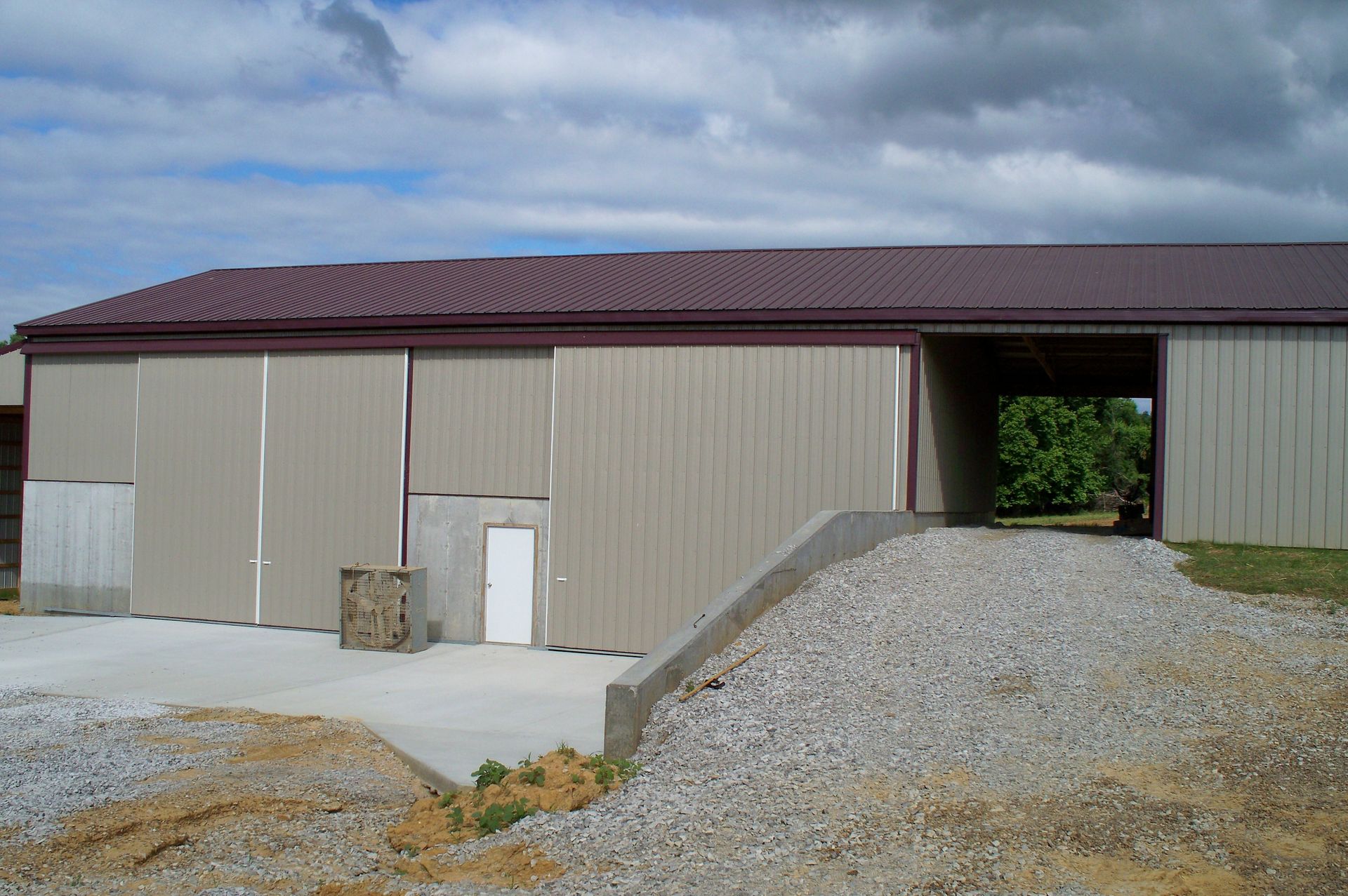 Large metal warehouse with a gravel ramp and open drive-through passage.