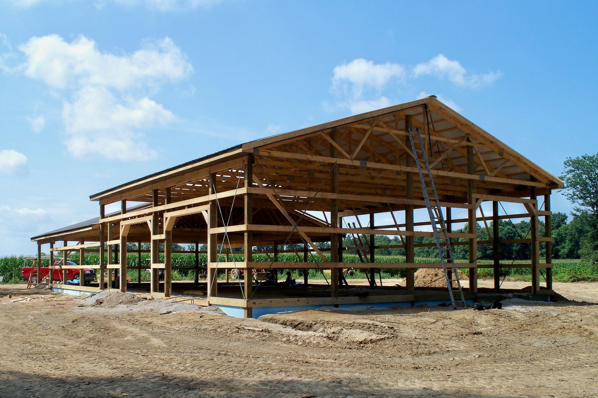 Partially built wooden pavilion frame on a dirt lot under a blue sky