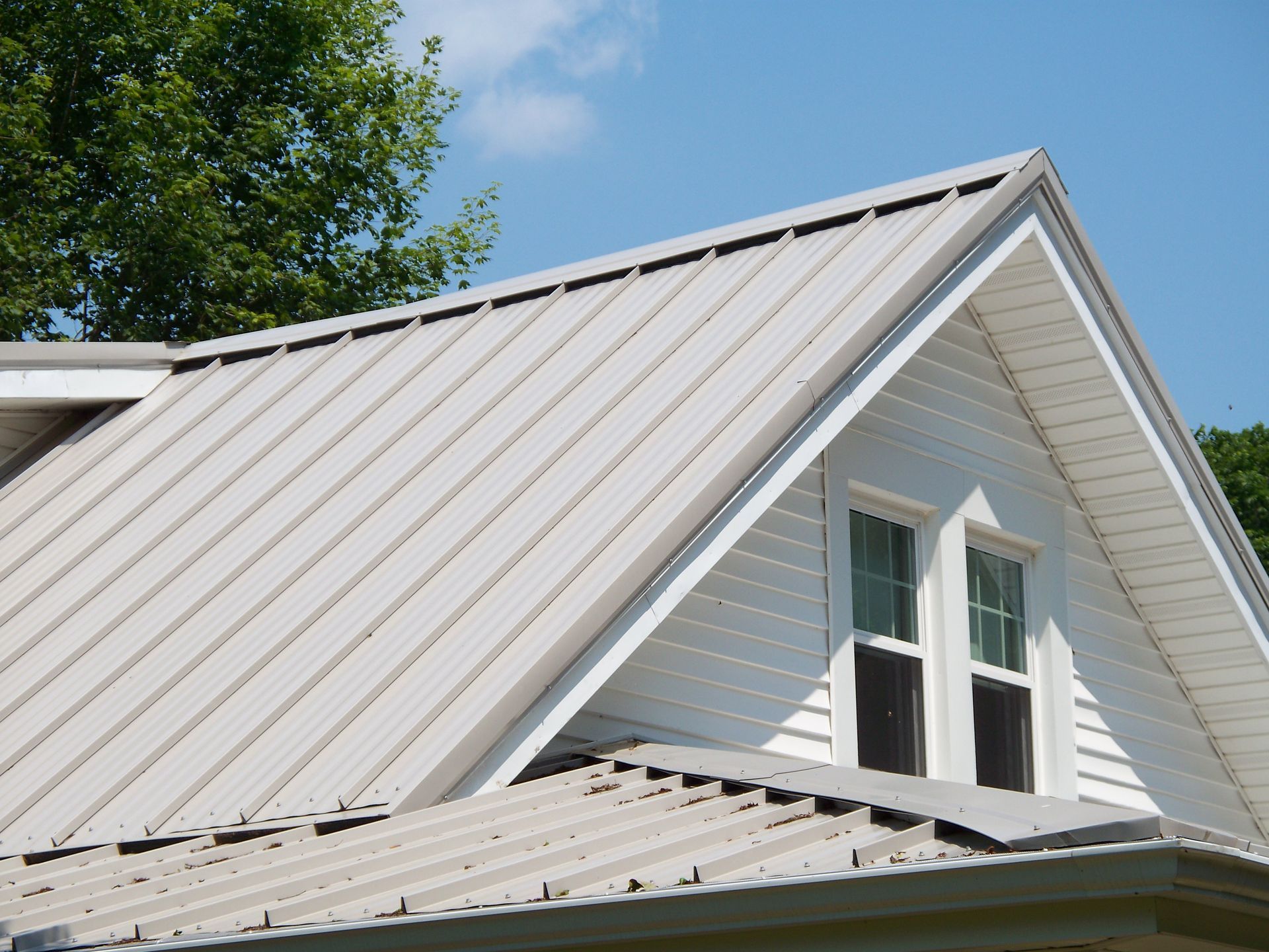 White metal roof and dormer window on a house under a blue sky