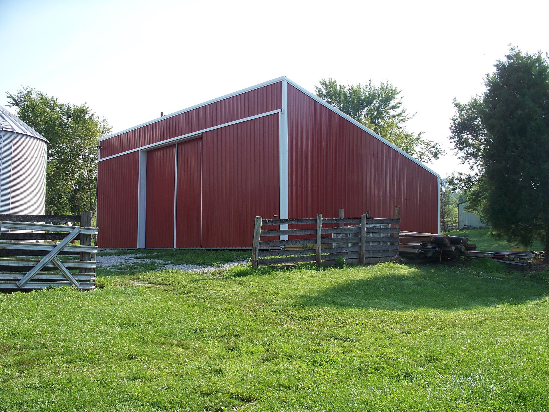 Red barn on a grassy field with wooden fences and trees in the background