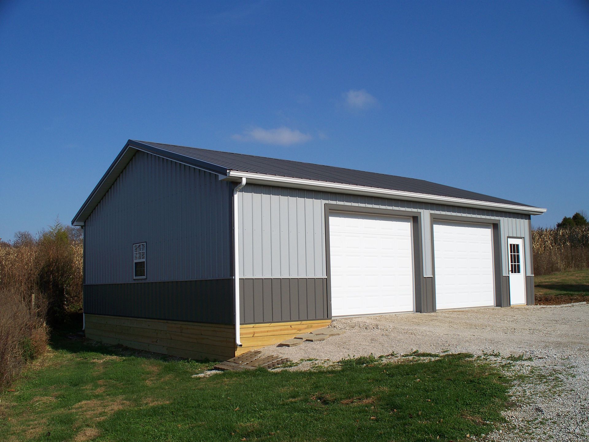 Gray metal garage with two white doors on a gravel driveway under a blue sky
