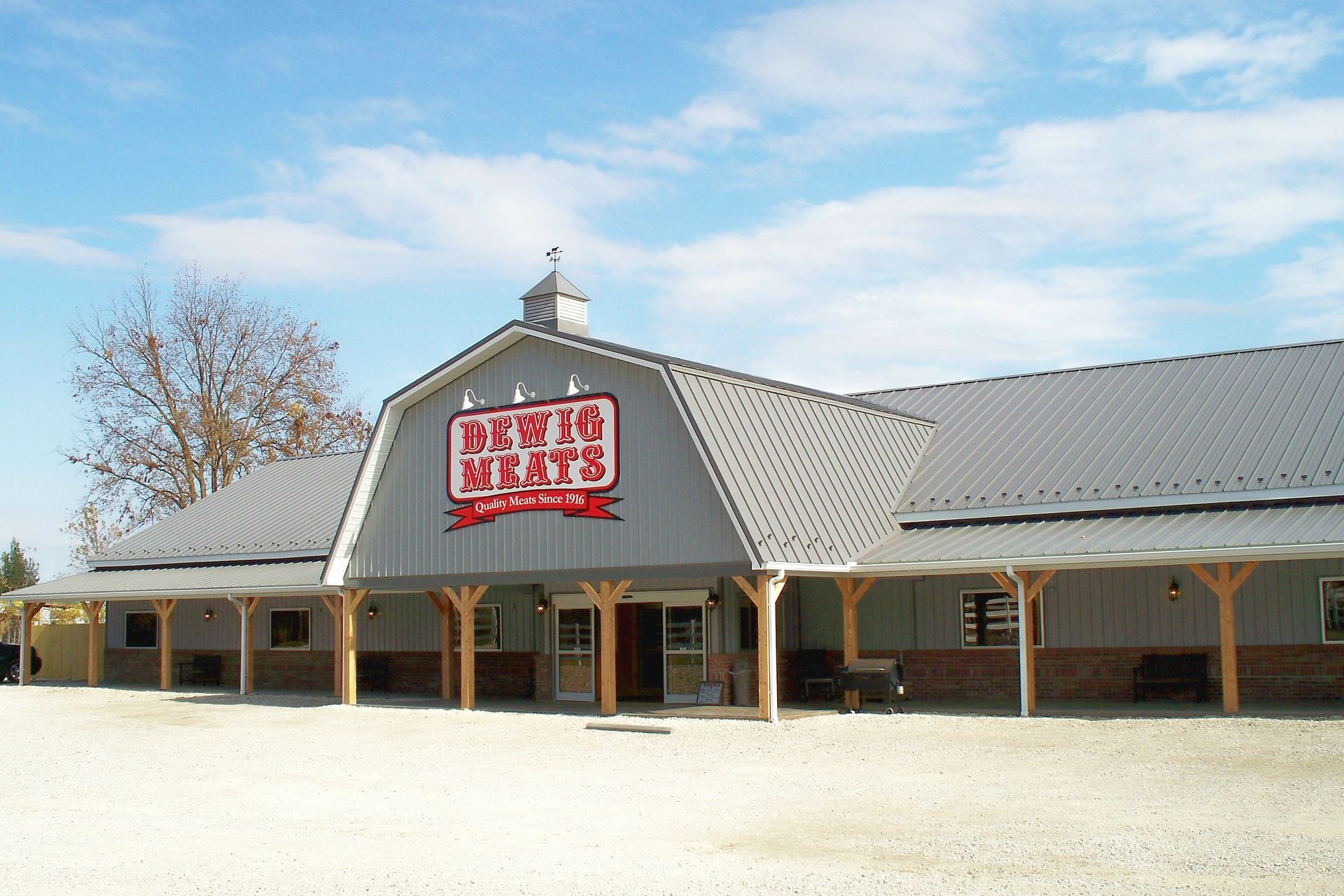 Rustic country store with gray metal roof and red sign under a blue sky