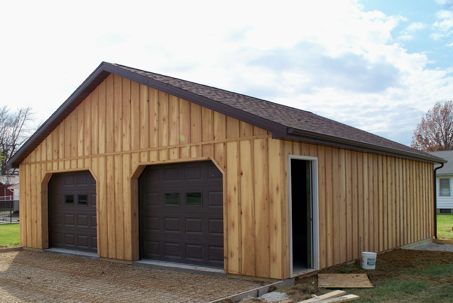 Wooden two-car garage with brown doors, a side entry door, and a gravel driveway