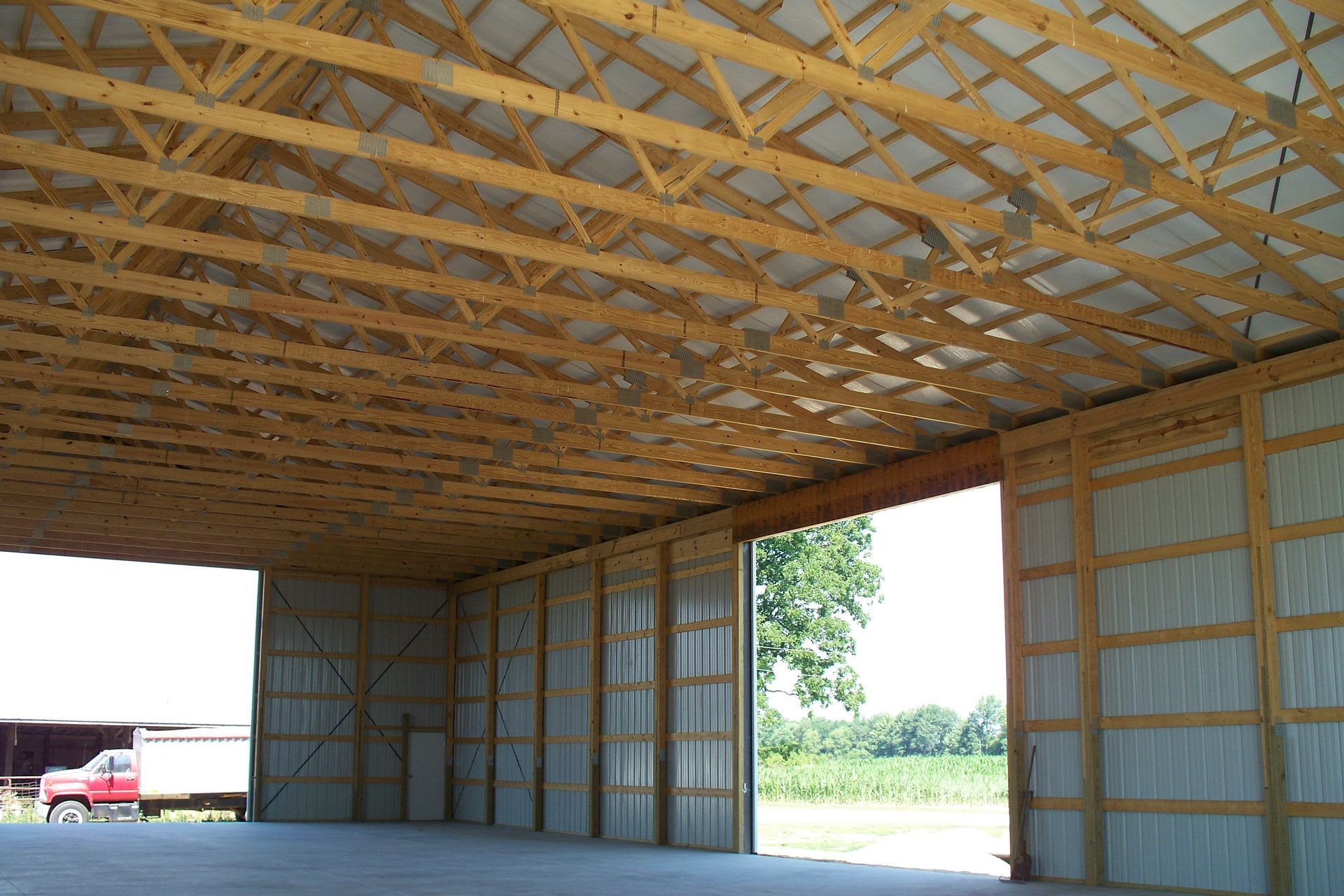 Empty unfinished wooden barn interior with exposed trusses and an open doorway to a grassy field