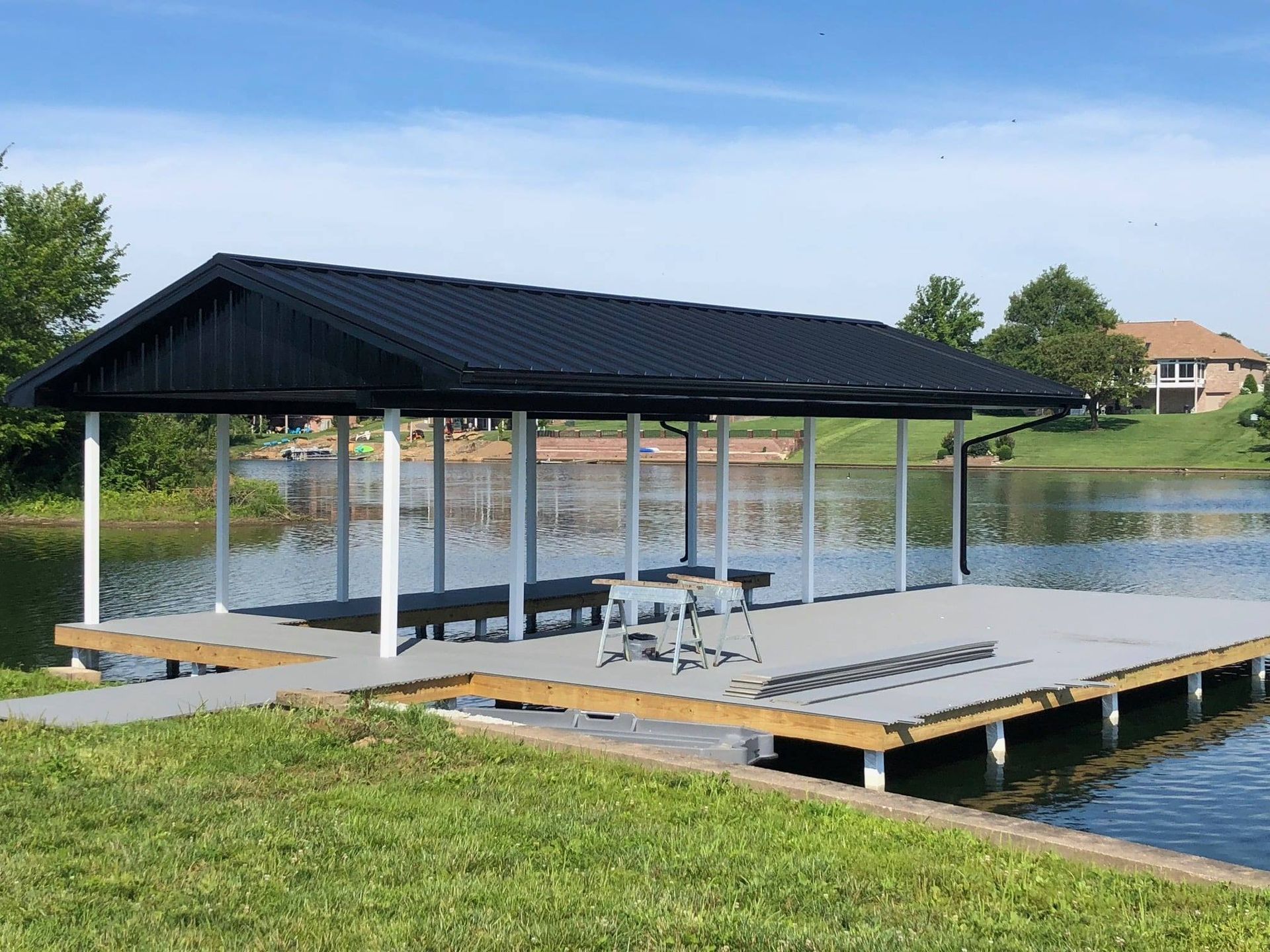 Covered lakeside dock with picnic tables, black roof, and wooden deck on calm water
