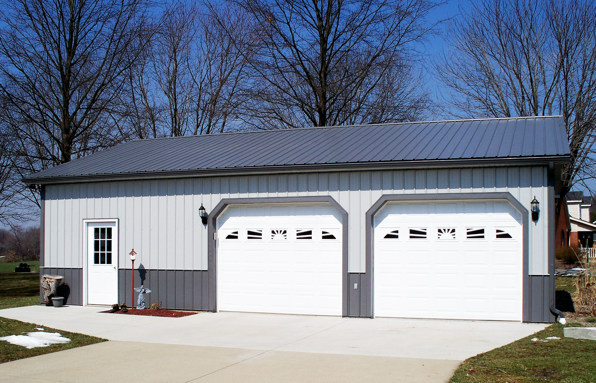 White two-car garage with gray roof and a side entry door, set on a driveway under a blue sky.