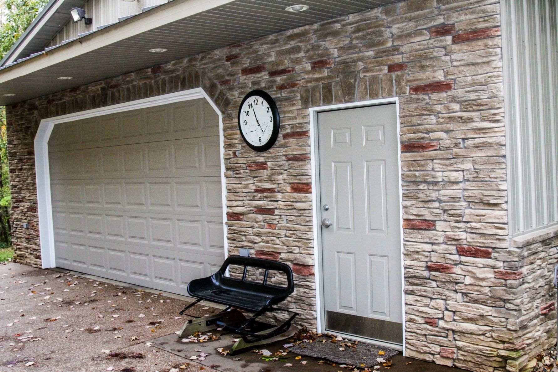 Garage exterior with white door, wall clock, and a broken black bench on stone siding