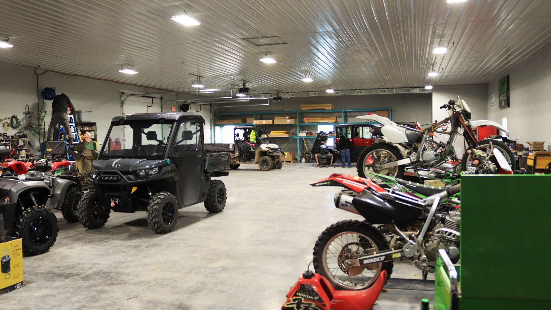 Garage with ATVs, dirt bikes, and off-road vehicles parked inside a bright workshop.