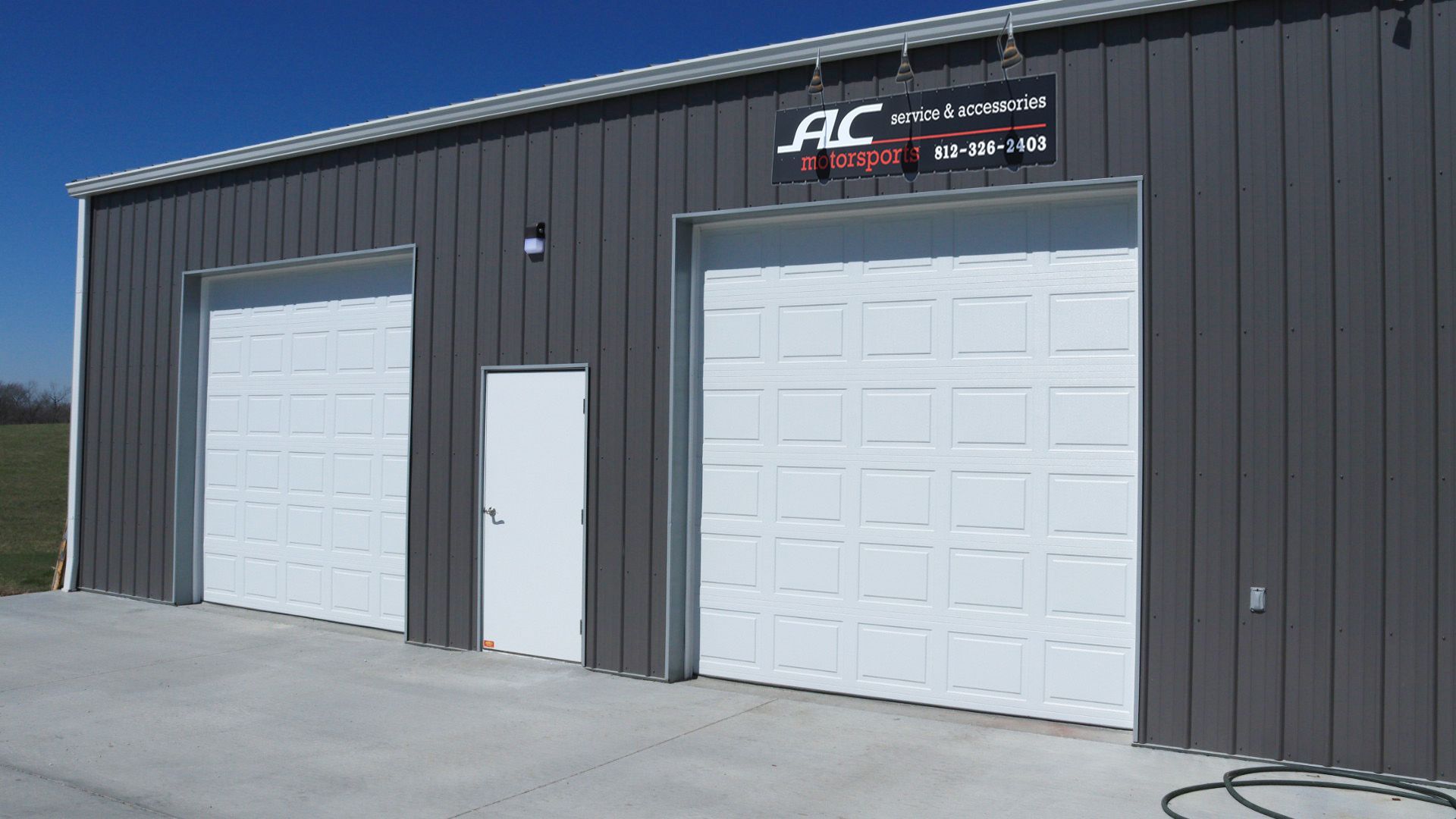 Two white garage doors on a gray metal building with an AC sign above the entrance.