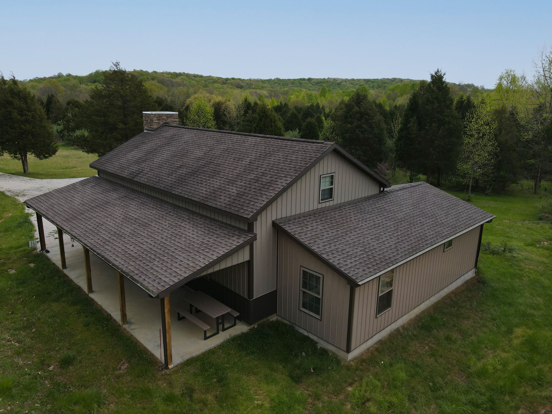 Aerial view of a gray house with a covered porch, surrounded by trees and grass.