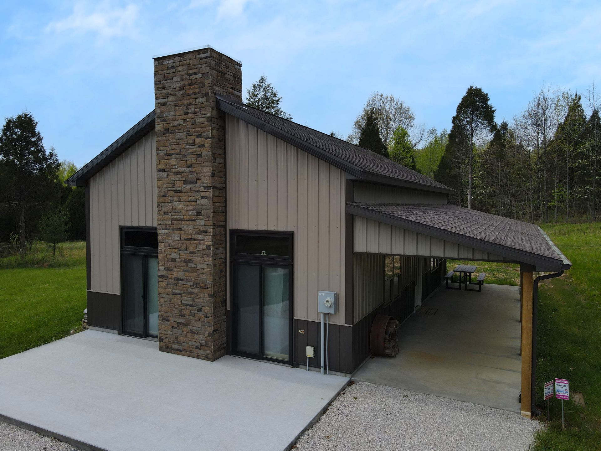 Modern house with stone and wood siding, sloped roof, and covered carport in a grassy wooded setting