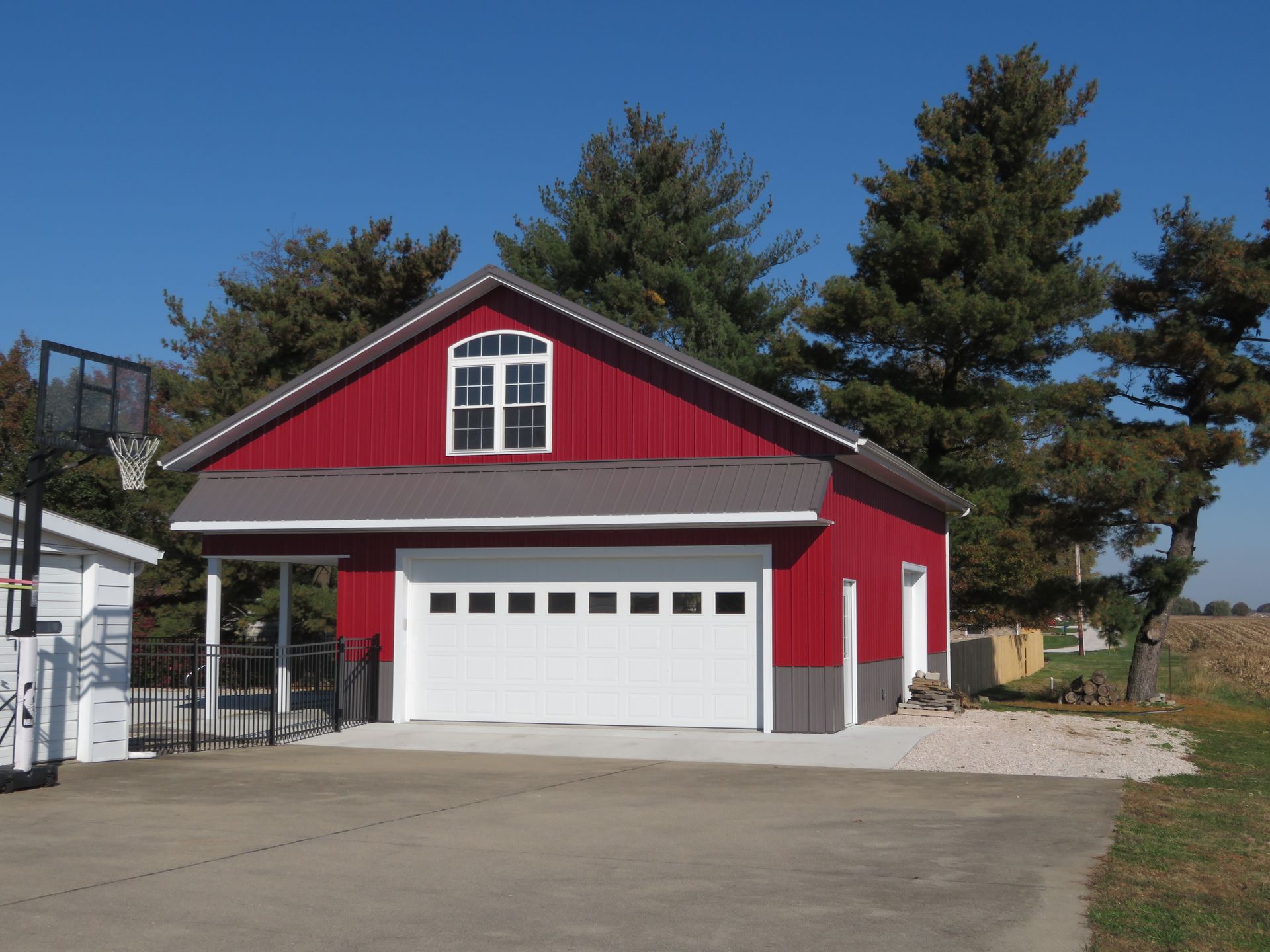 Red two-story garage with white doors and trim in a driveway, surrounded by trees.