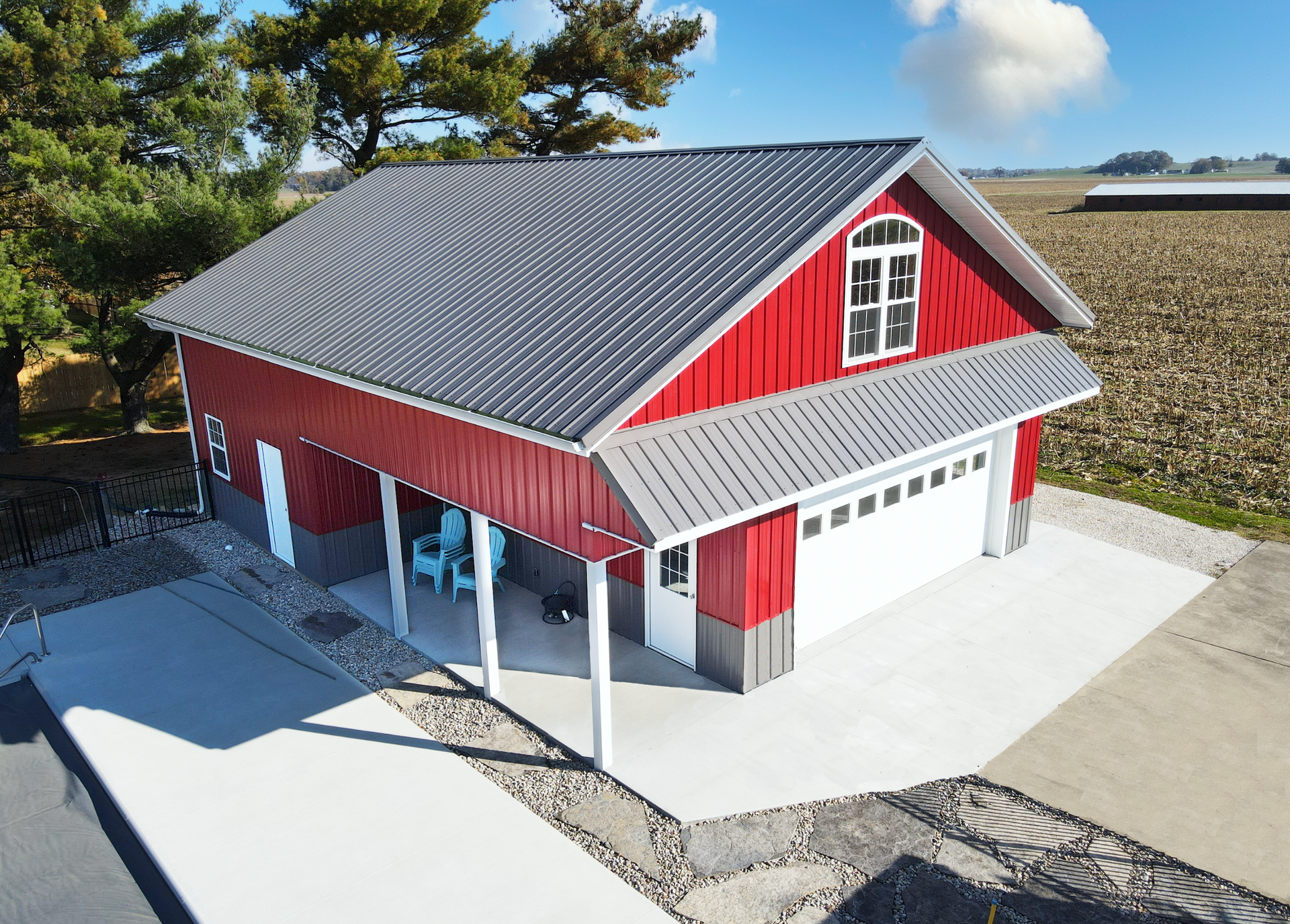 Red barn-style garage with gray roof and white trim on a paved driveway, viewed from above.