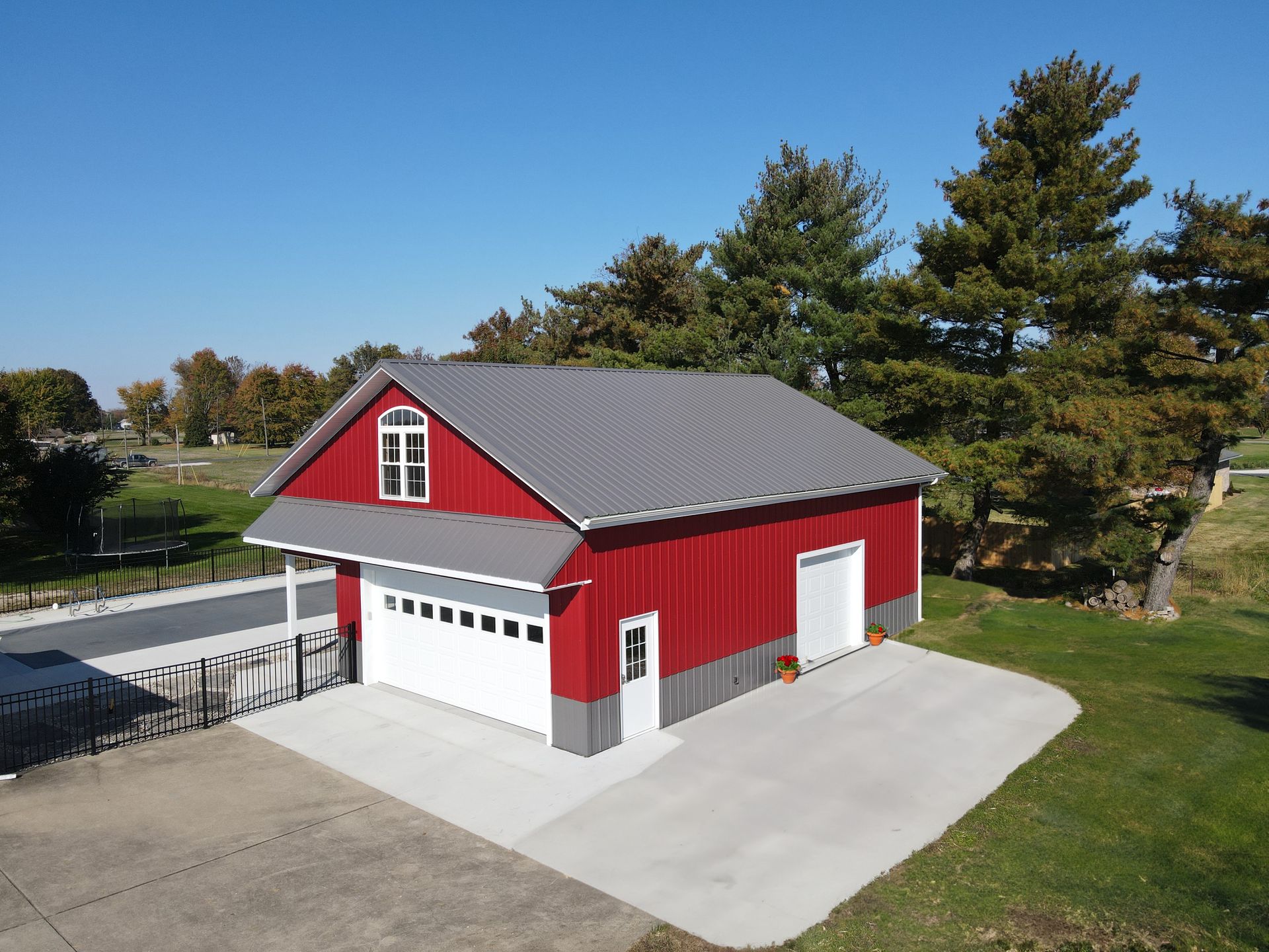 Red barn-style garage with white doors and trim on a paved driveway under a clear blue sky.