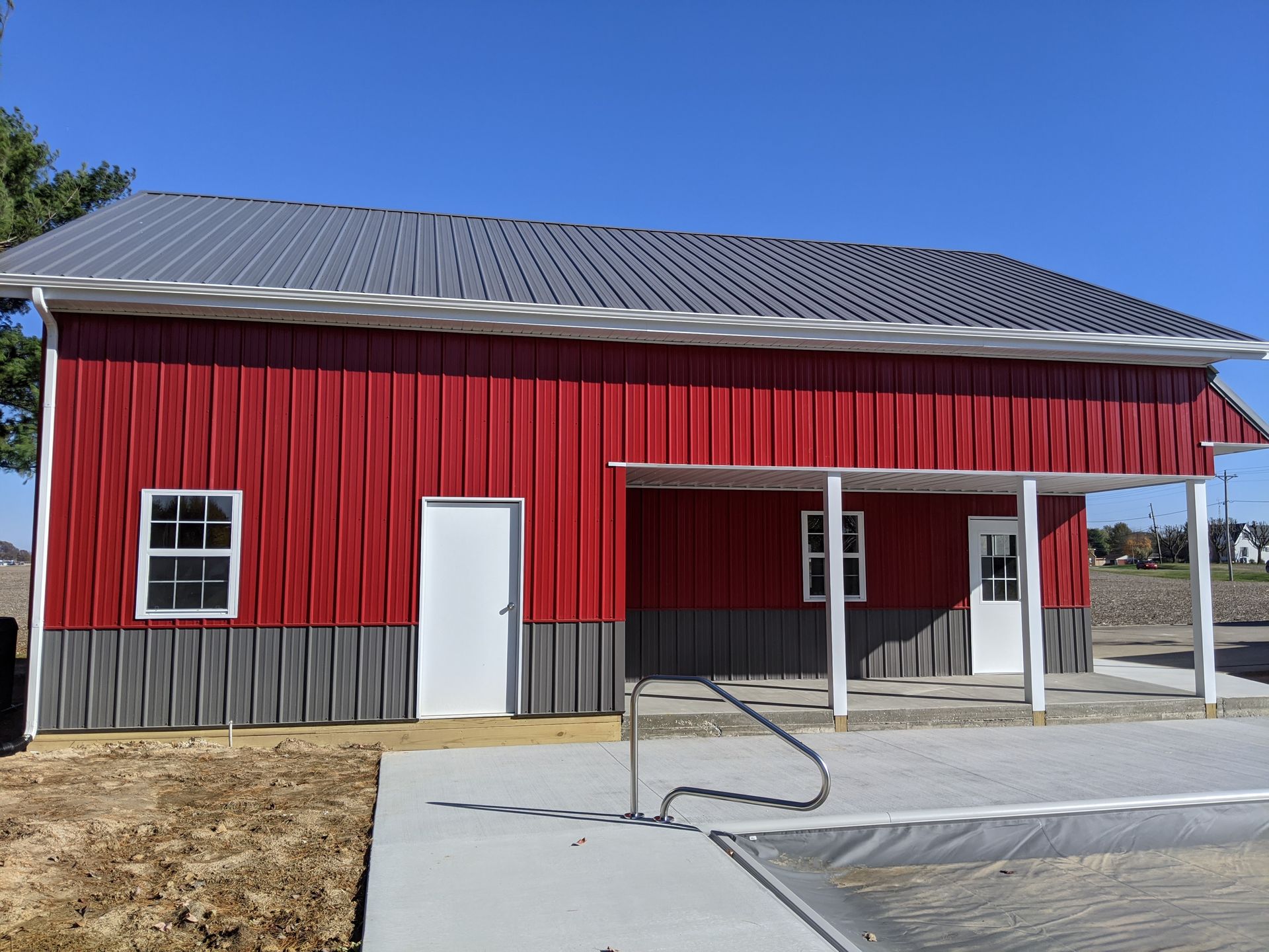 Red barn-style building with white trim, a metal roof, and a covered entrance on a concrete pad