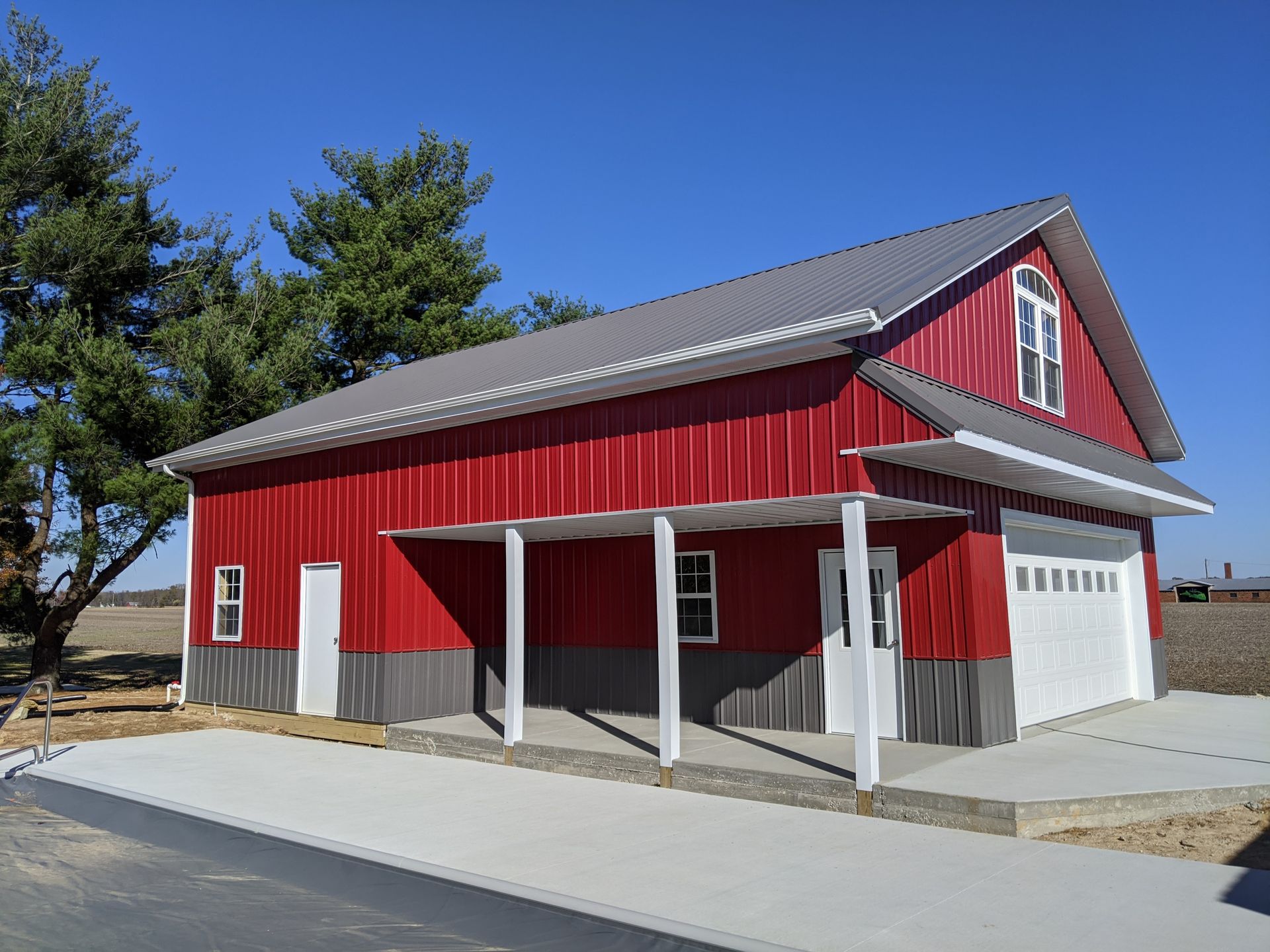 Red barn-style building with white trim and a gray roof on a paved lot under a blue sky