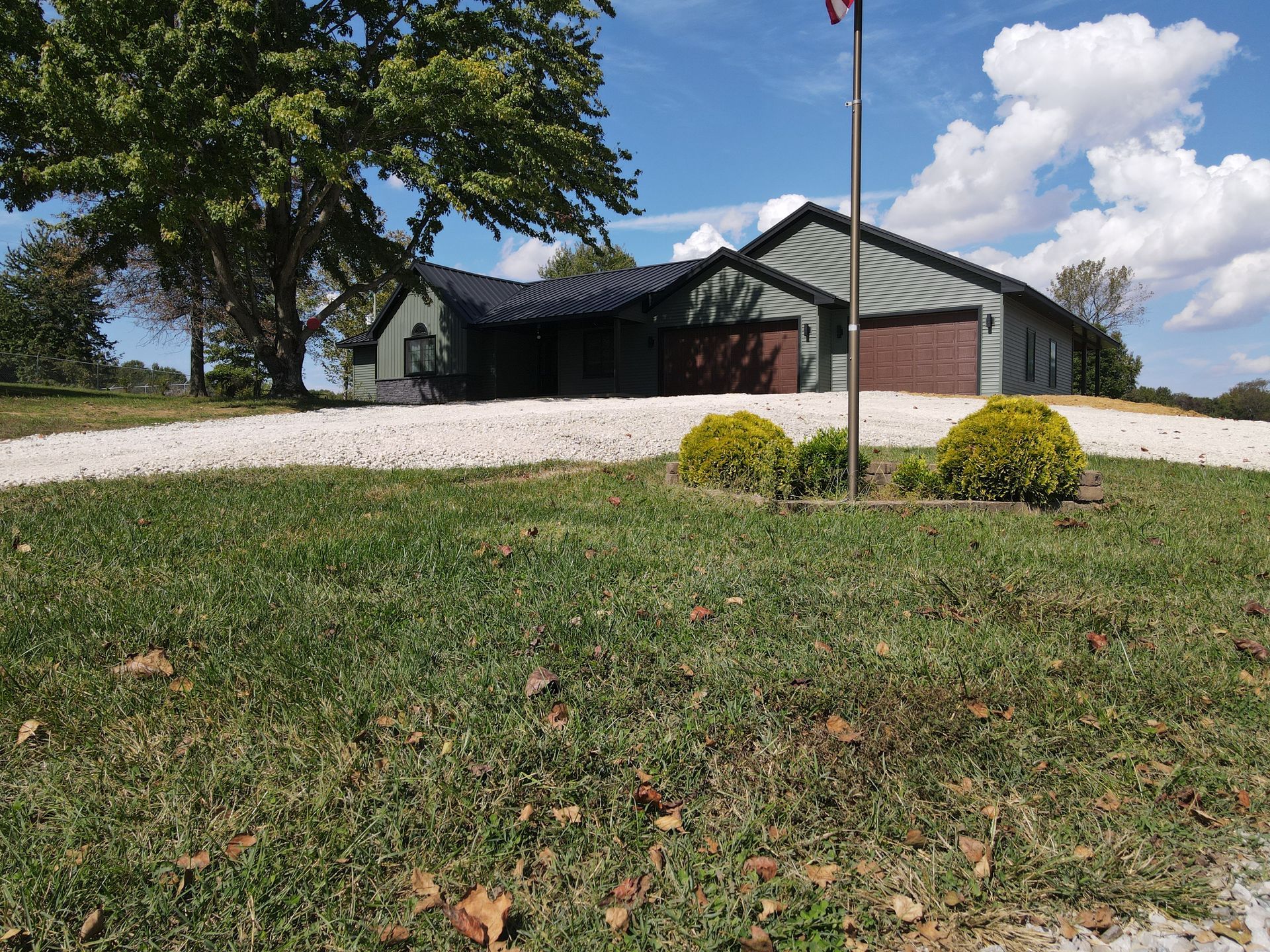 Single-story brick house with a gravel driveway, front lawn, and flagpole on a sunny day