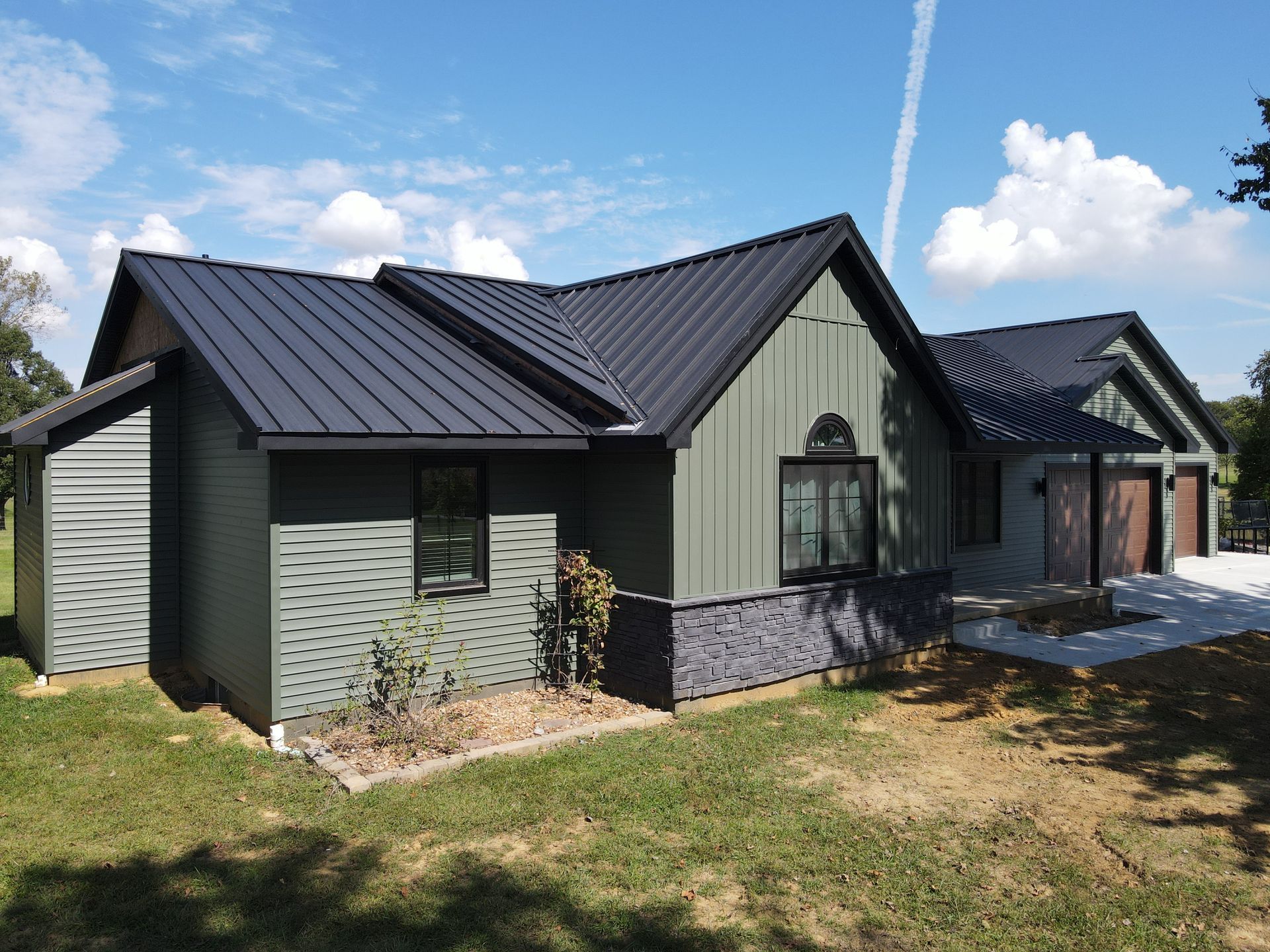 Modern dark-green house with black roof and stone base under a blue sky